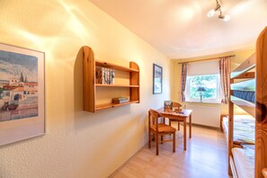 Ein Zimmer mit einer Holzhülle, einem gerahmten Bild, einem Tisch mit Stuhl und einem Etagenbett.