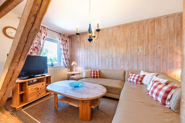 Ein gemütliches Wohnzimmer mit Holzbalkendecke, einer Couch, einem Fernseher und einem Tisch mit einer blauen Schüssel.