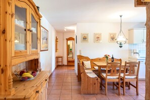 Ein Essbereich mit Holztisch und -stühlen, einem Schrank mit Glastüren sowie einer im Hintergrund sichtbaren Küche.