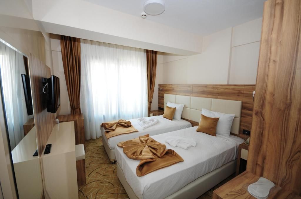 A hotel room with two beds, a TV, a wooden headboard, and a window with curtains.