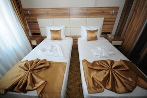 Ein Hotelzimmer mit zwei Betten, jeweils mit einem Holzkopfstück, weißer Bettwäsche und einer braunen Zierrose.