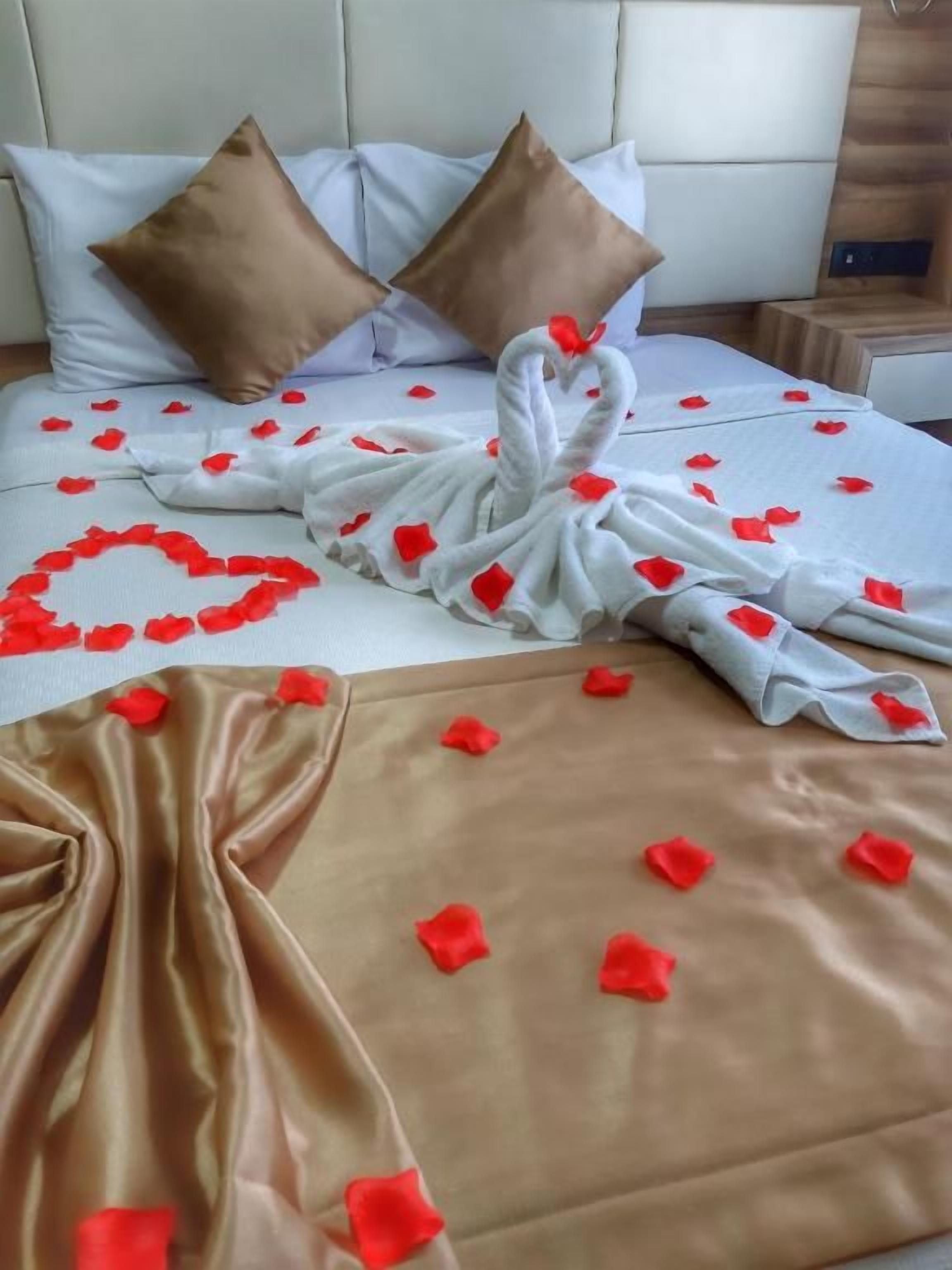 Ein Bett mit einer herzenförmigen Anordnung aus Rosenblättern und einem Handtuch.