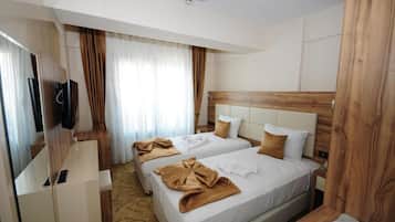 A hotel room with two beds, a TV, a wooden headboard, and a window with curtains.