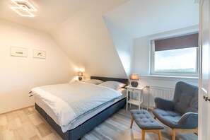 Ein Schlafzimmer mit einem Bett, Nachttischen, einem Sessel und einem Fenster.