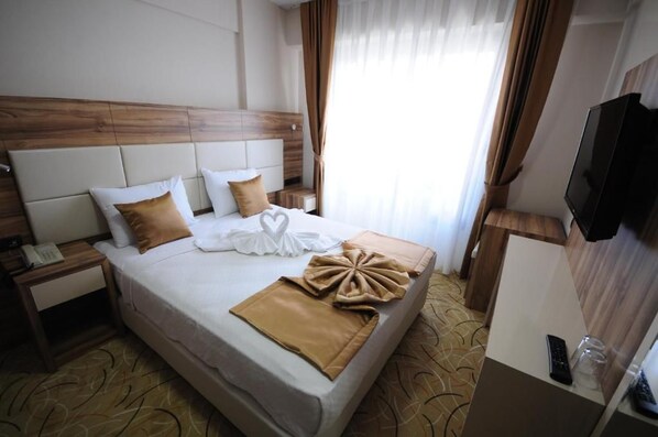 Ein Hotelzimmer mit einem Bett, einem Nachttisch mit Telefon, einem an der Wand befestigten Fernseher und einem Fenster mit Vorhängen.