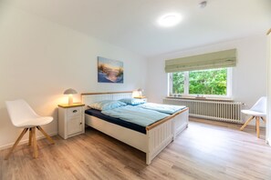 Ein Schlafzimmer mit Bett, Nachttischen, einem Sessel, einem Fenster mit Blick ins Grüne und einem Bild an der Wand.