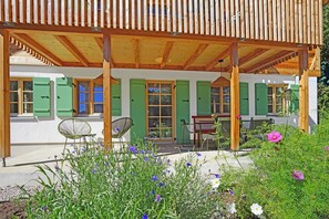 Eine Holzhütte mit einer überdachten Terrasse, grünen Fensterläden und Außenmöbeln.