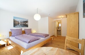 Ein Schlafzimmer mit Bett, Nachttischen, einer Hängeleuchte, einem Holzschrank und einem Badezimmer mit Spiegel und Waschbecken.