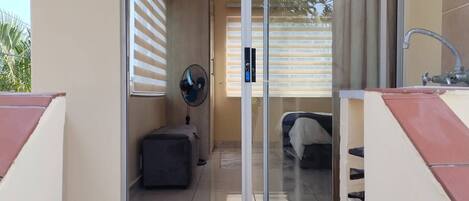A hotel room with a sliding glass door leading to a balcony, a small fan, a suitcase, and a bed.