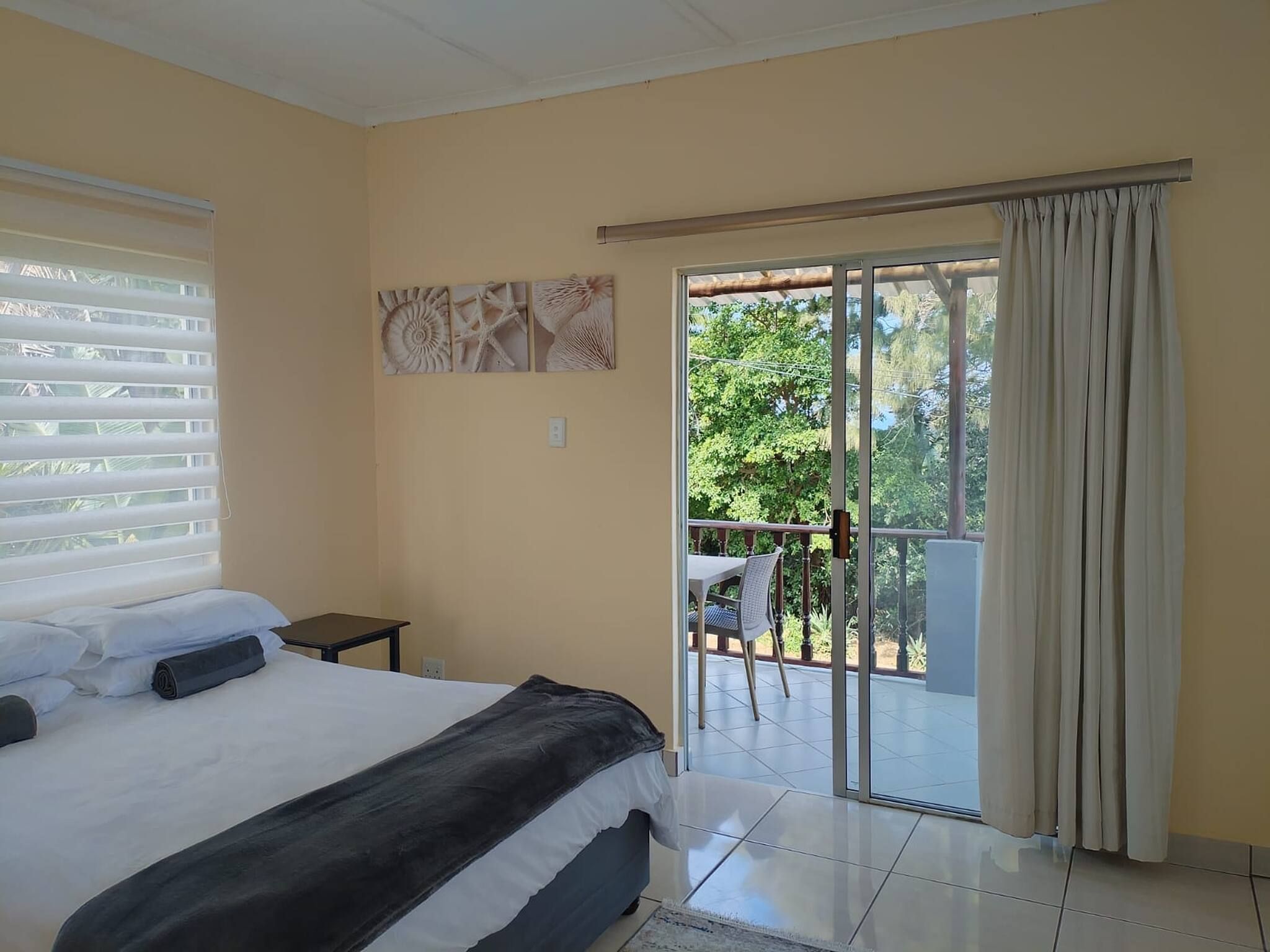 A bedroom with a bed, a small table, and a balcony with a chair.
