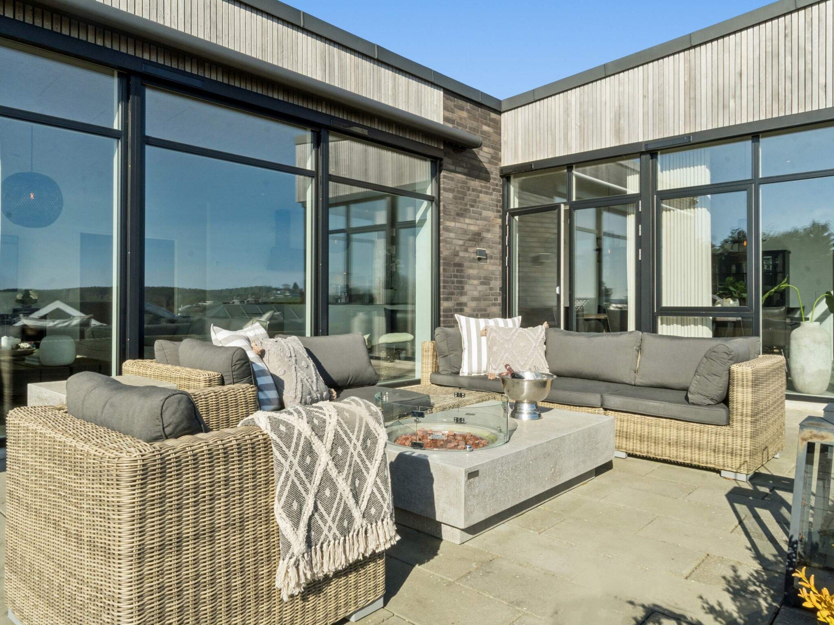 An outdoor seating area with wicker furniture, a glass coffee table, and a stone fireplace.