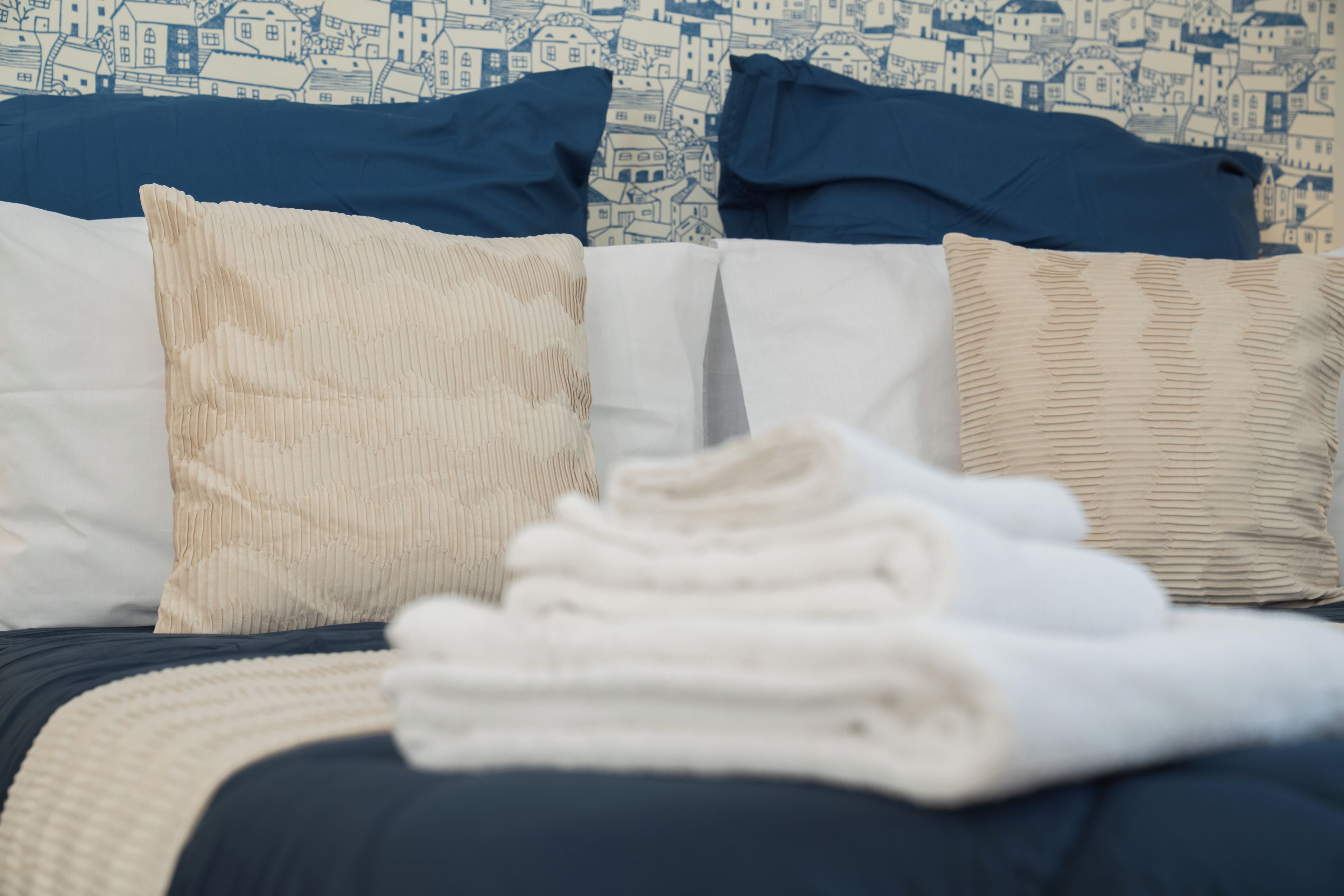 A bed with a blue and white patterned headboard, a white pillow, a beige pillow, and a folded white towel.