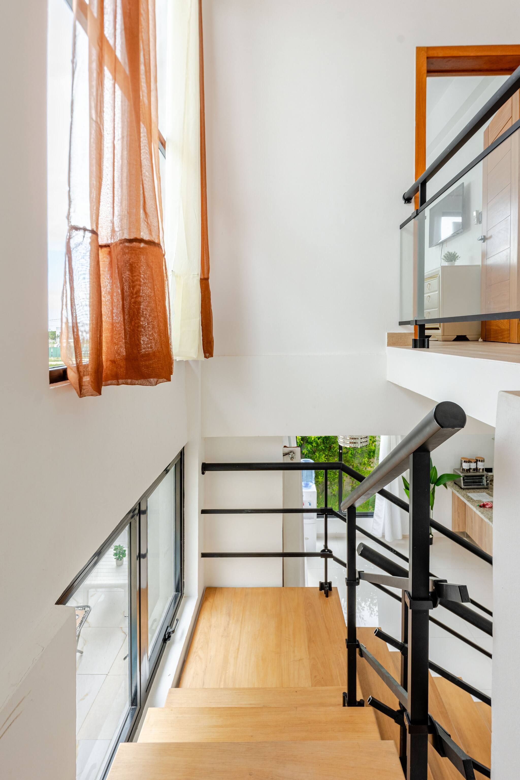 A narrow staircase with wooden steps and black metal railings, leading to a second-floor landing with a view of greenery outside.