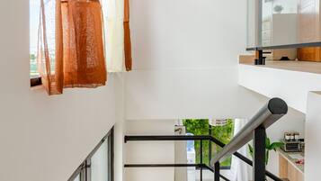 A narrow staircase with wooden steps and black metal railings, leading to a second-floor landing with a view of greenery outside.