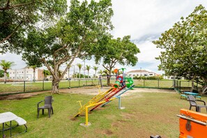 A playground with slides and swings, surrounded by trees and a fenced area. - Beautiful place 12 minutes from airport (Punta Cana)
