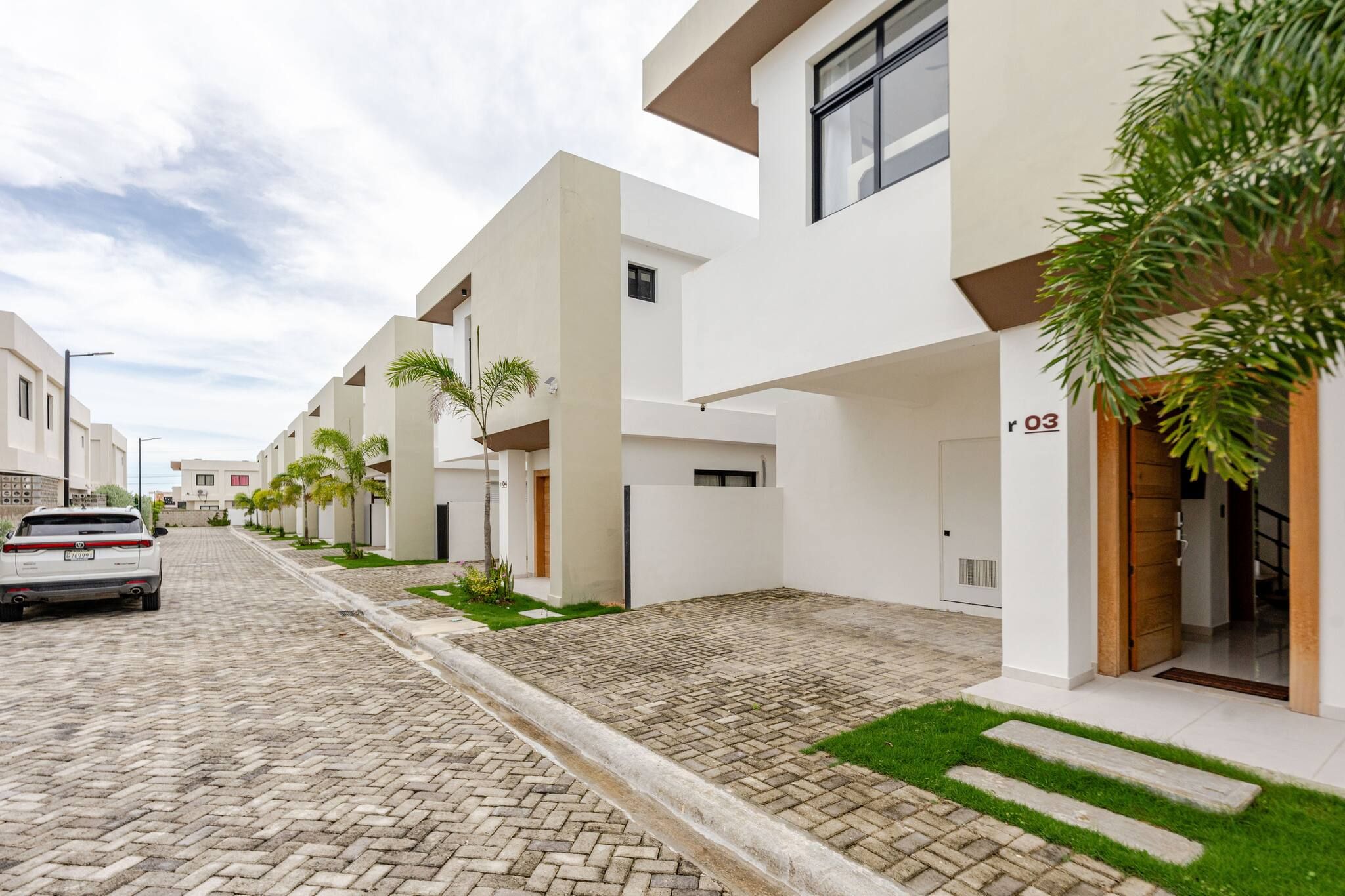 A modern residential street with white buildings, a paved road, and a parked car.