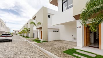 A modern residential street with white buildings, a paved road, and a parked car.