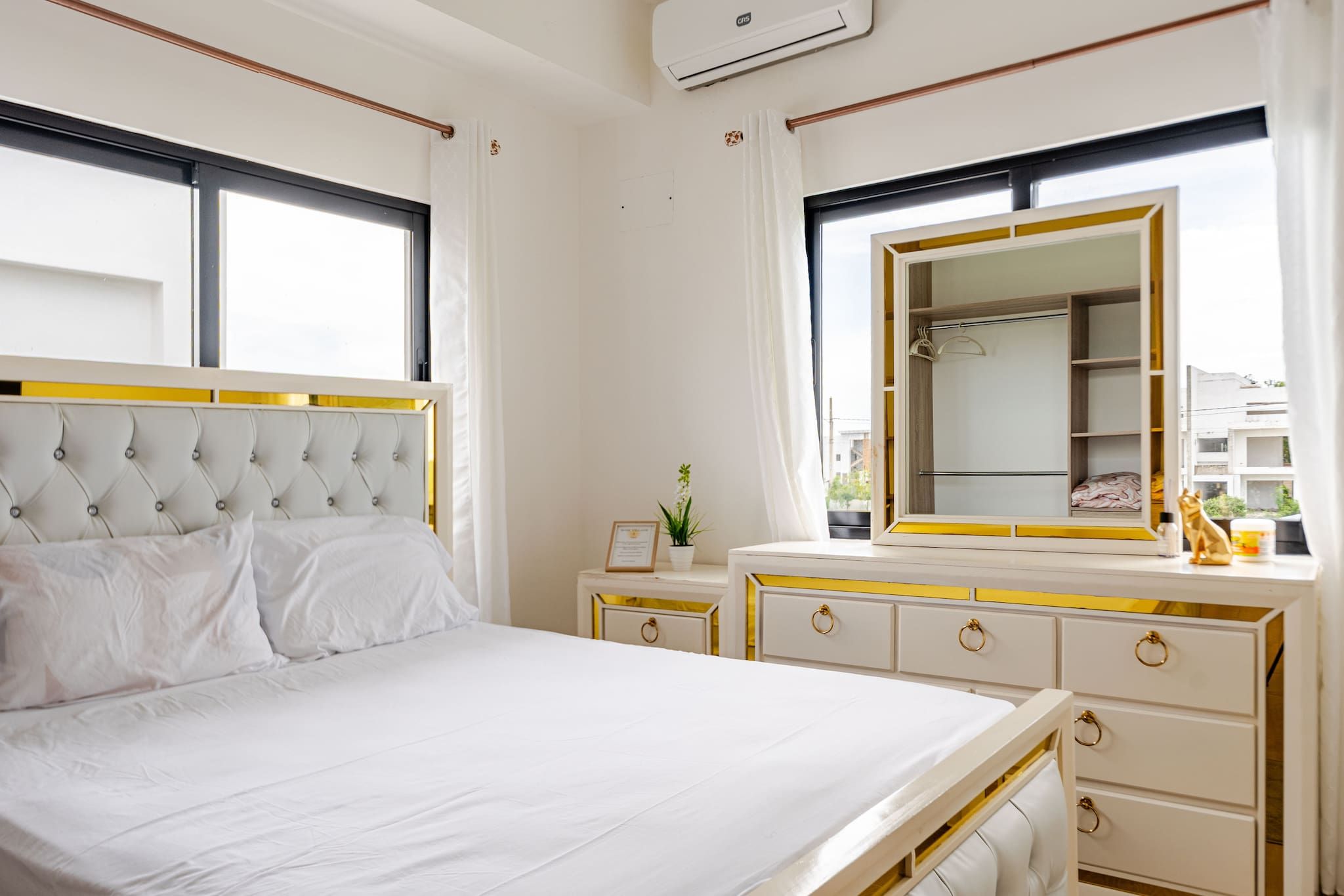 A hotel room with a large bed, bedside tables, a dresser, a mirror, and a window with curtains.