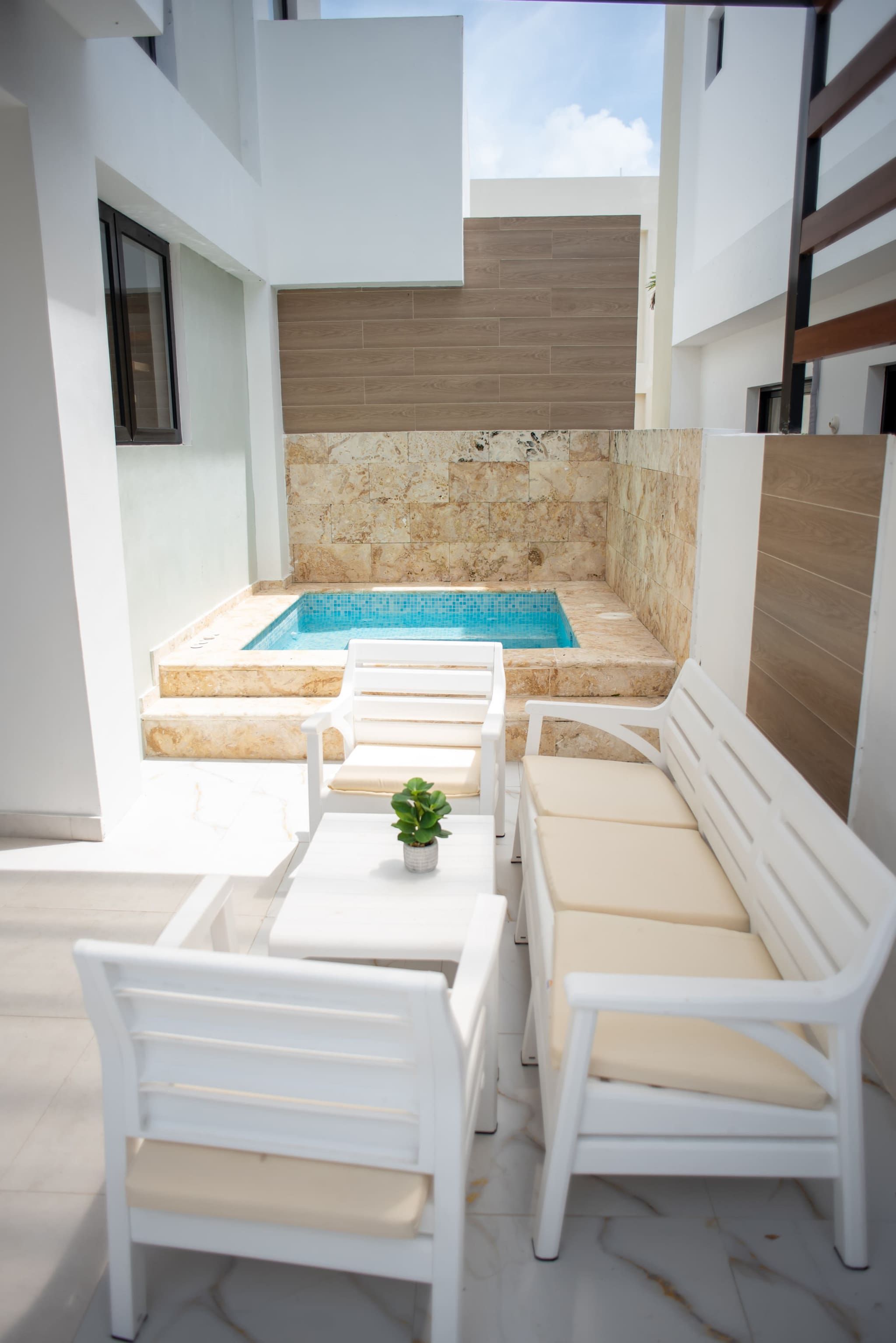 A modern outdoor pool area with a rectangular pool, white lounge chairs, and a small potted plant.
