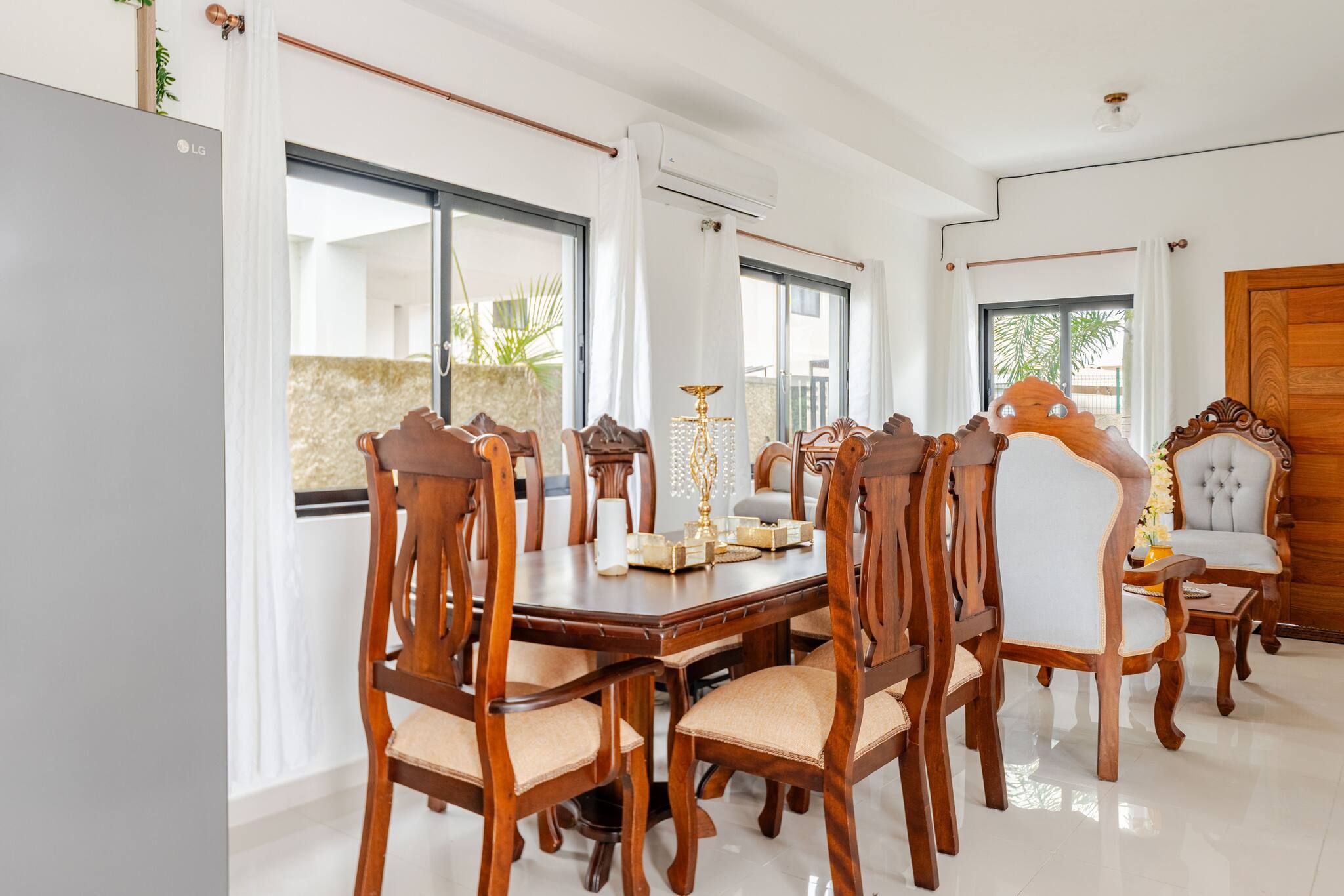 A dining area with a wooden table and chairs, large windows, and an air conditioning unit.
