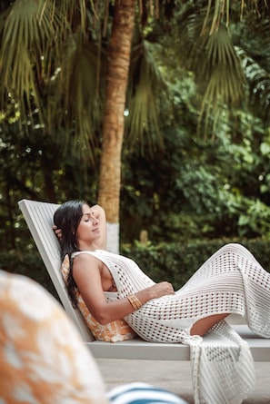 Uma pessoa relaxada em uma espreguiçadeira em um cenário tropical, com vegetação exuberante ao fundo.
