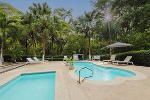 Une piscine entourée de palmiers et de verdure, avec des chaises longues et des parasols.