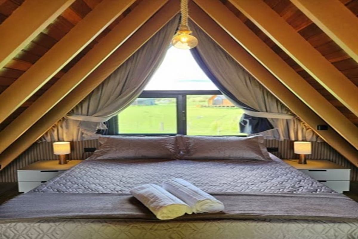 Ein Schlafzimmer mit einem großen Bett, zwei Nachttischlampen und Blick auf eine grüne Landschaft durch ein Fenster.