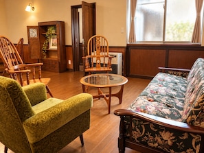 A room with a wooden floor, a green patterned sofa, a floral patterned sofa, a glass-top coffee table, and two wooden chairs with intricate designs. - KUROKOCHI STAY (Nakamachi, Aizuwakamatsu-shi)