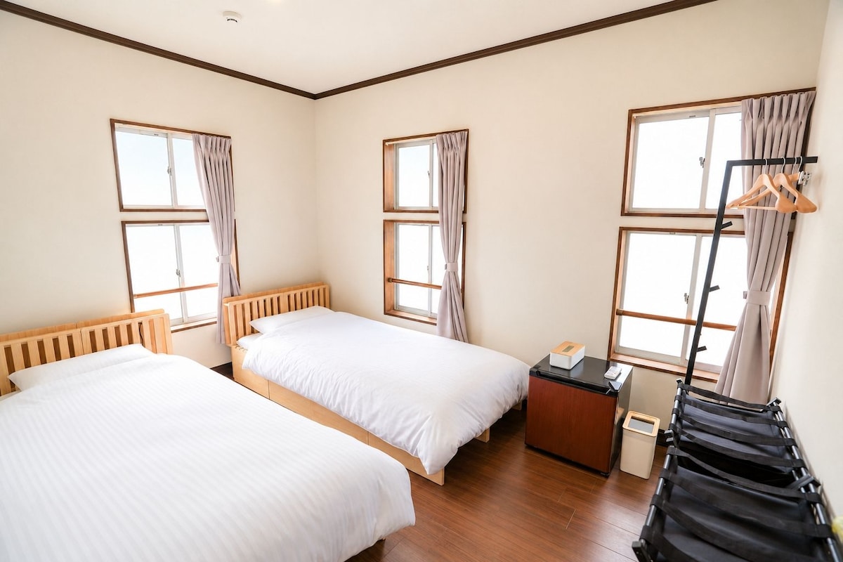 A hotel room with two beds, a small desk, and a wardrobe.