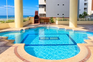 A swimming pool with a tiled edge, a wooden deck, and a view of a building with balconies. - New Listing (Cartagena de Indias)
