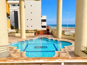 A swimming pool with a tiled deck, a barbecue area, and a view of the beach and ocean. - New Listing (Cartagena de Indias)