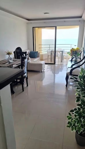Una sala de estar moderna con comedor, sofá y balcón con vista al mar.