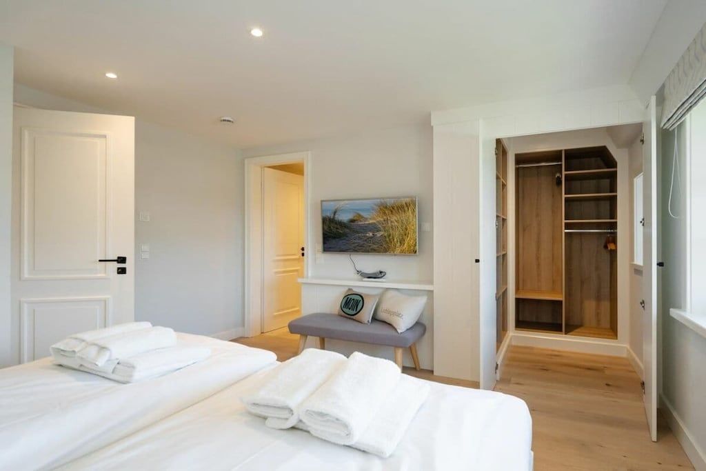 A hotel room with two beds, a bench, a painting, and a walk-in closet.