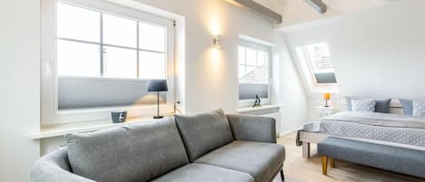Un dormitorio moderno con un sofá gris, una cama con edredón gris y una ventana con vista a un edificio.