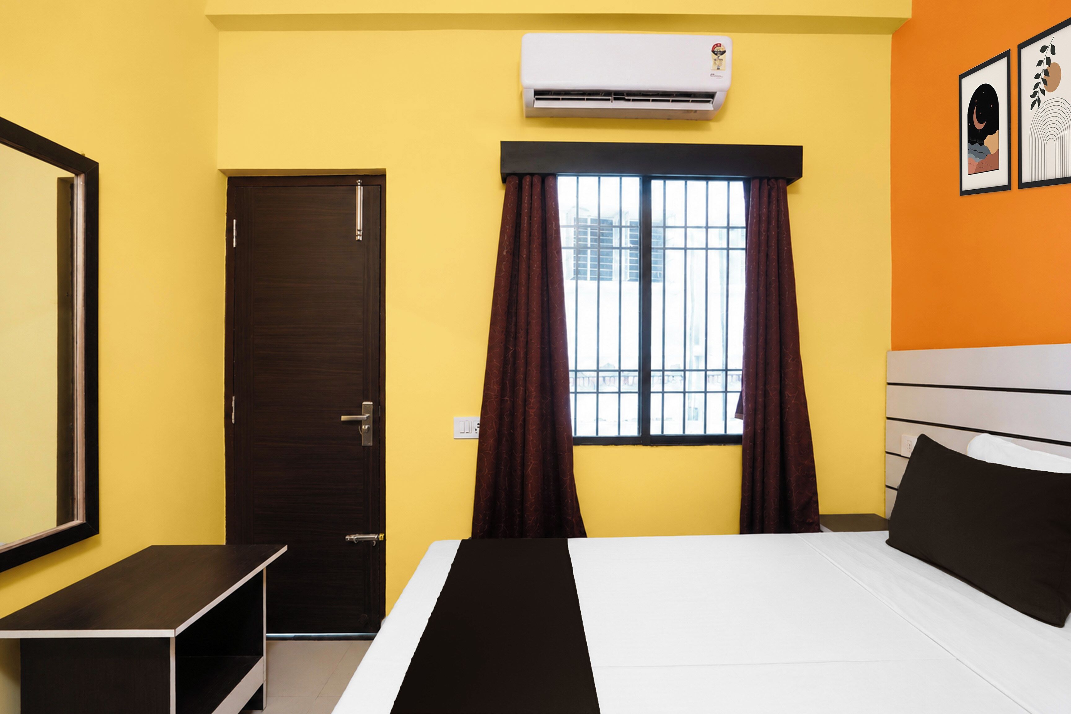 A hotel room with a bed, a window with curtains, an air conditioning unit, and a door.