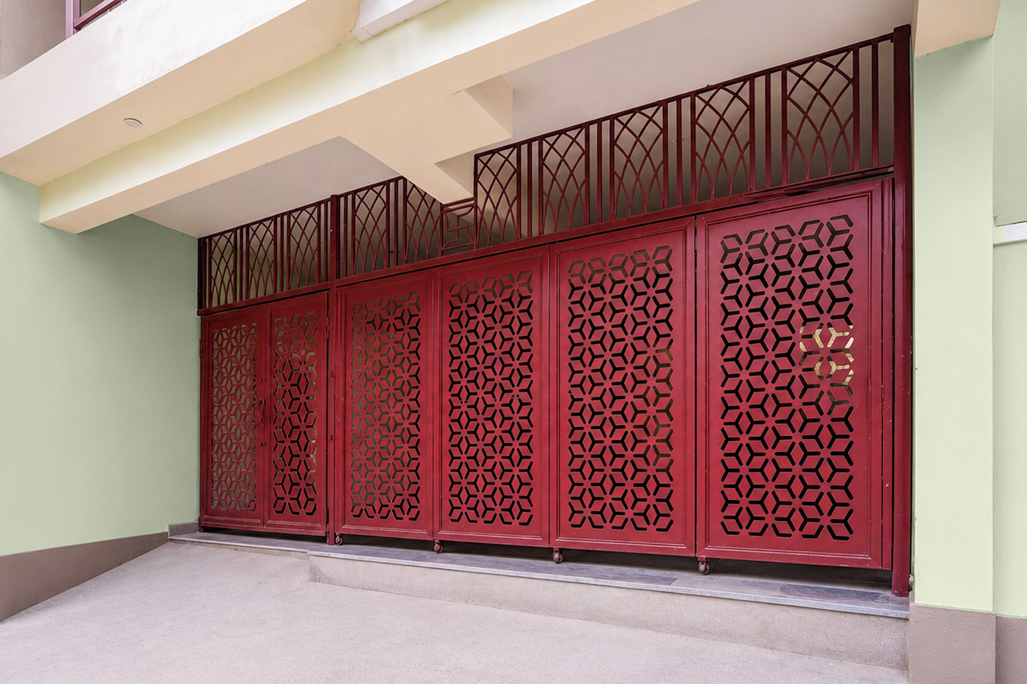 A red gate with intricate cut-out patterns, a balcony with a white railing, and a light green wall.