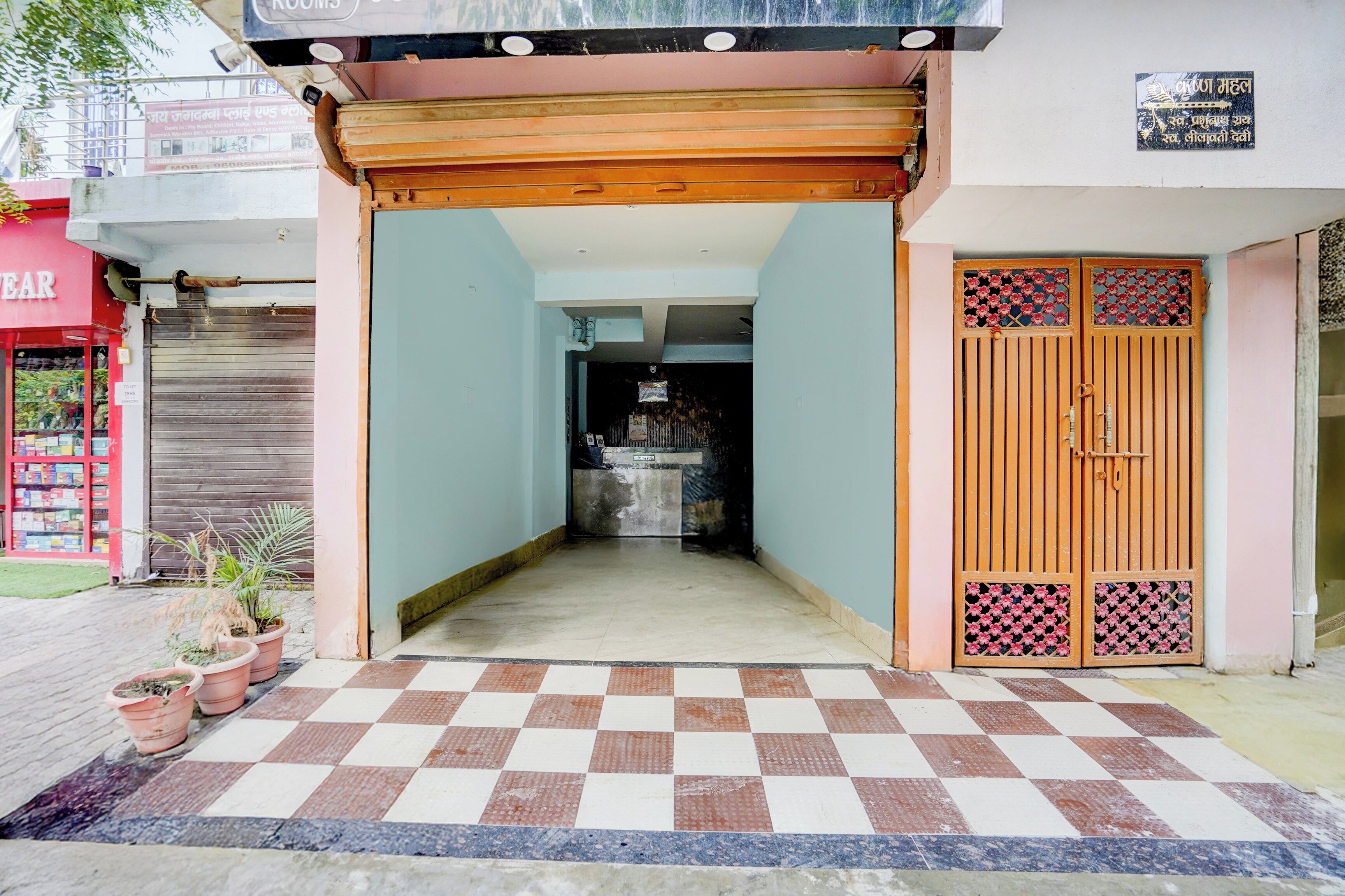 Une entrée d’immeuble avec un sol à carreaux, un espace d’accueil et une porte en bois ornée de panneaux décoratifs.