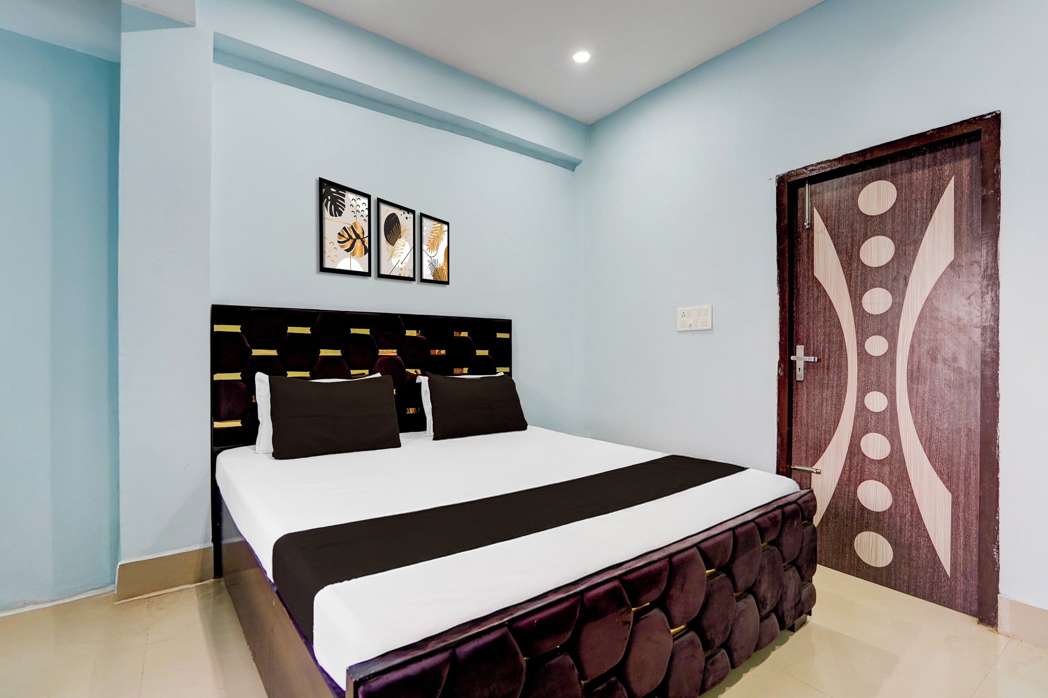 Un dormitorio con cama, cabecera, una puerta y cuadros colgados en la pared.