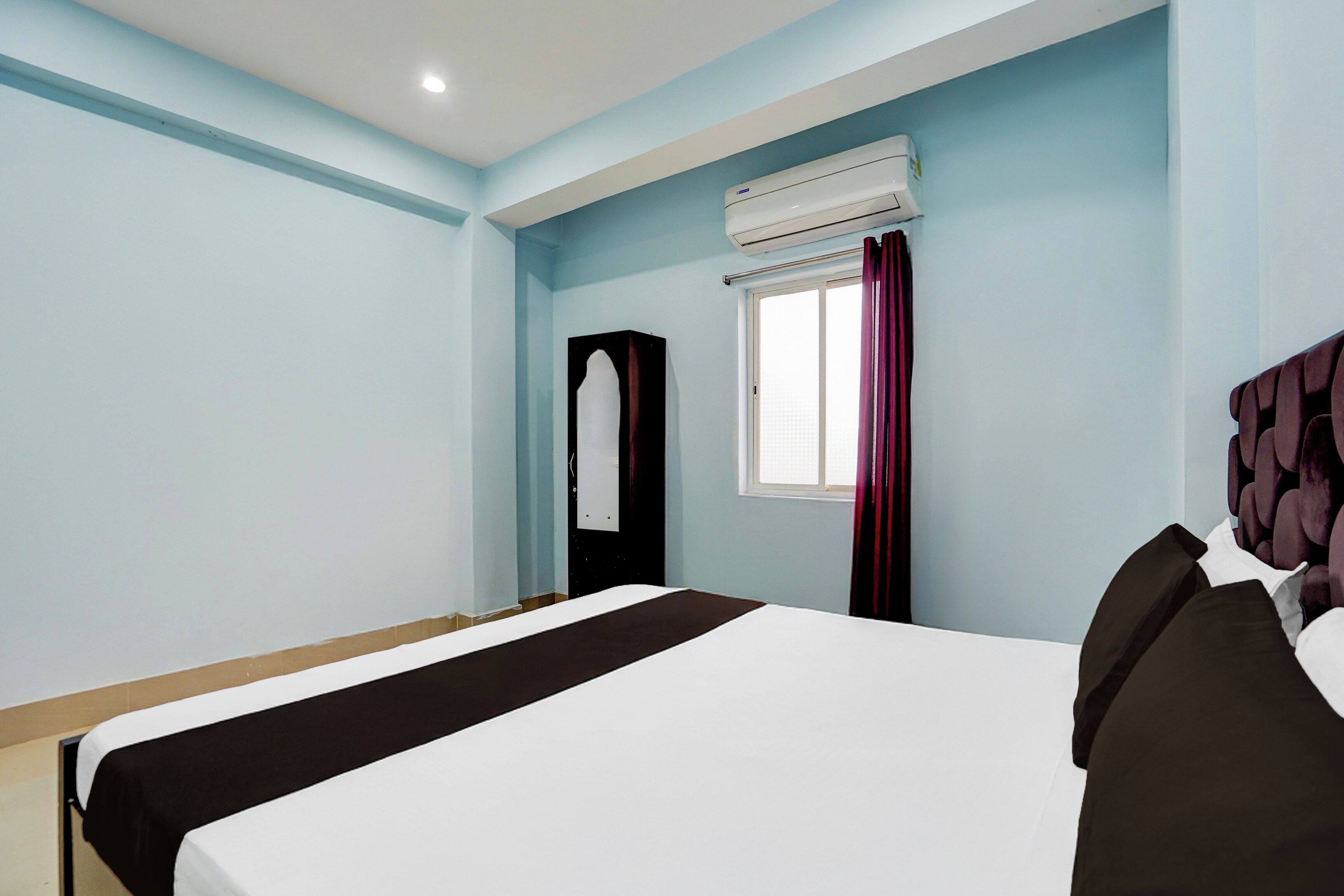 Une chambre d’hôtel avec un lit, une fenêtre avec des rideaux, un appareil de climatisation et une porte dotée d’un miroir.