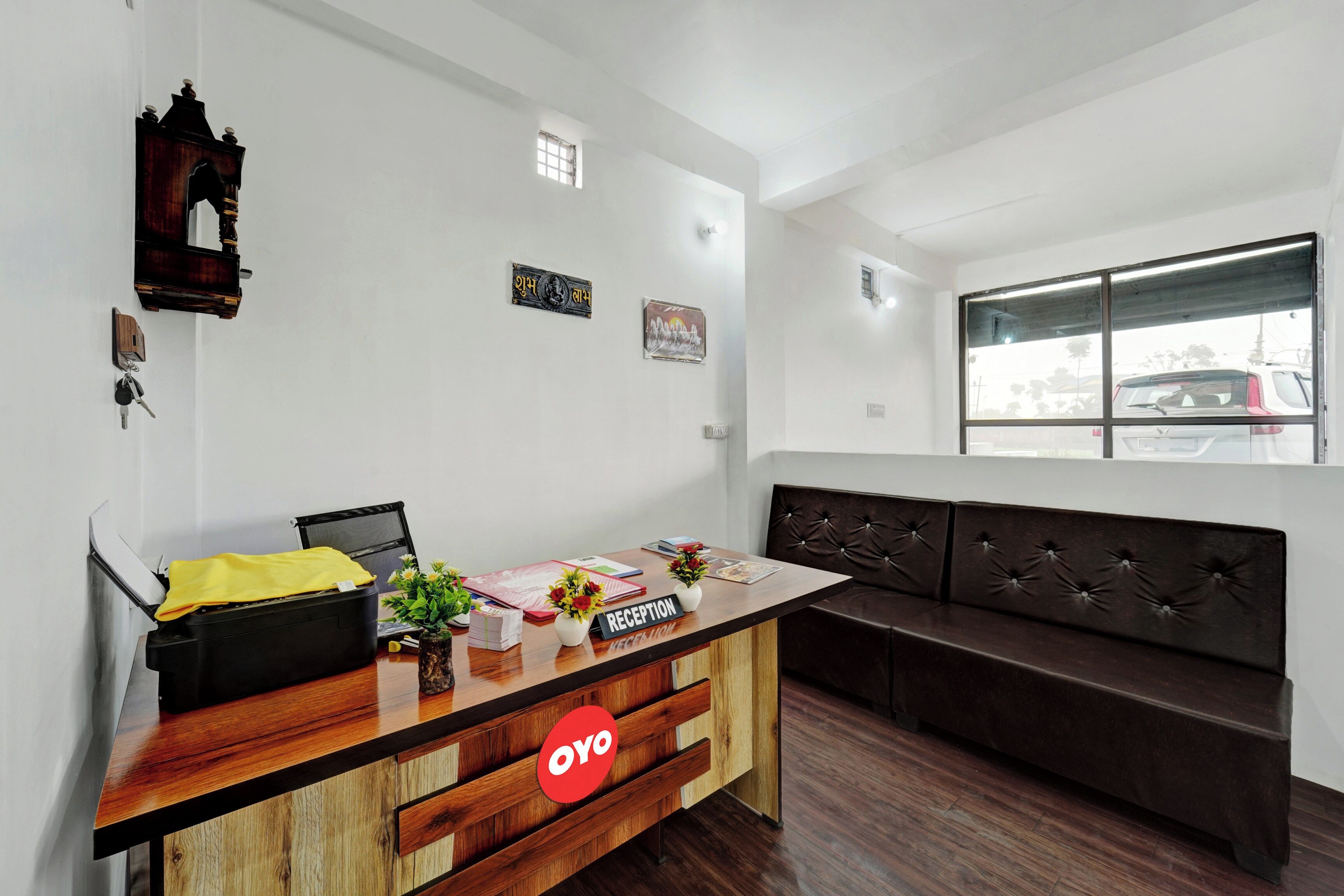 A reception desk with a wooden finish, a bench, and a window with a view of parked cars.