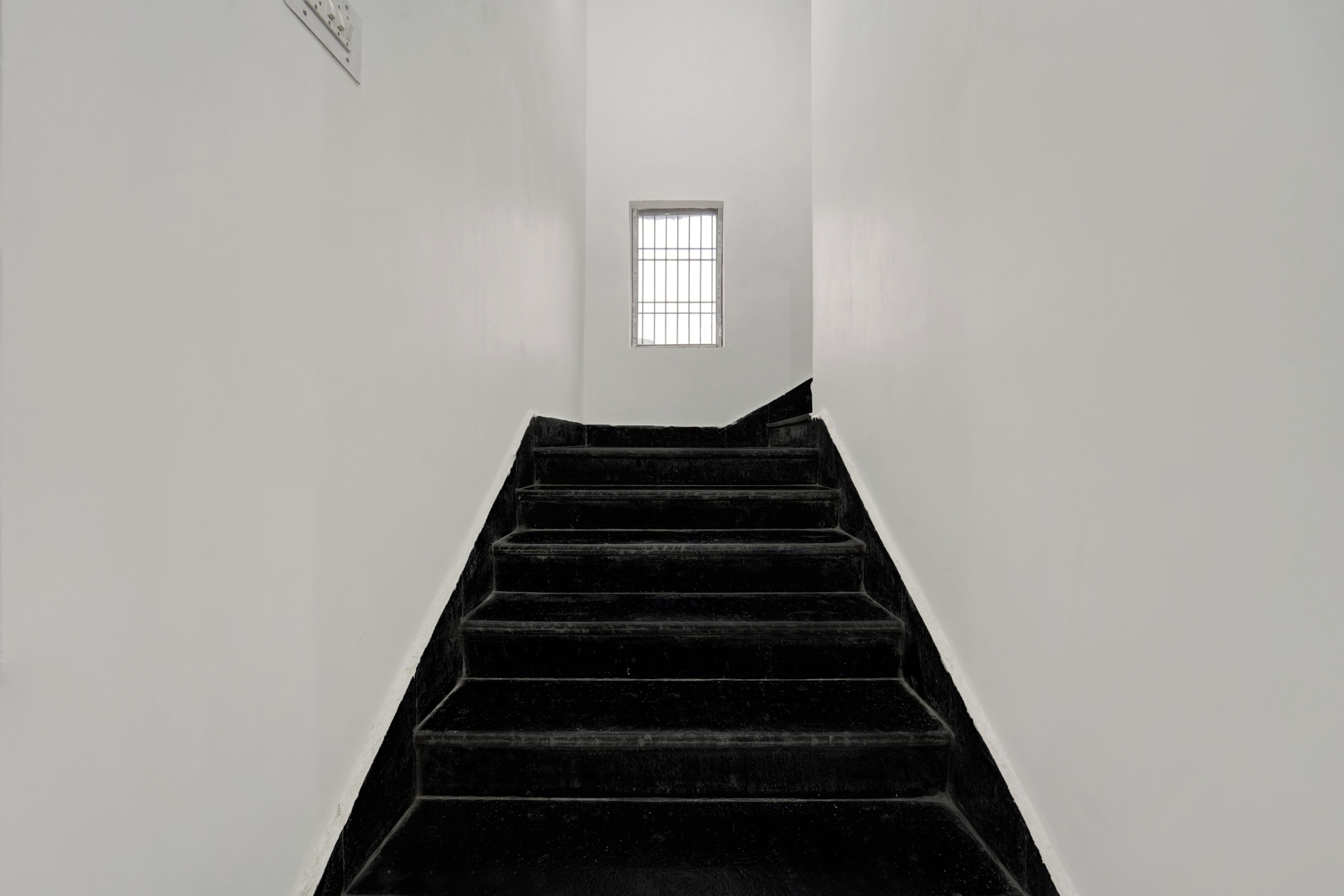 A staircase leading to a window with a grid pattern, surrounded by plain walls.
