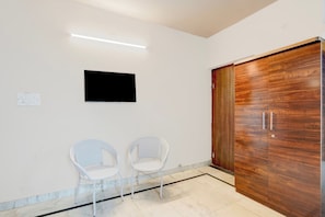 Una habitación con un armario de madera, dos sillas de mimbre, un televisor montado en la pared y un interruptor de luz.