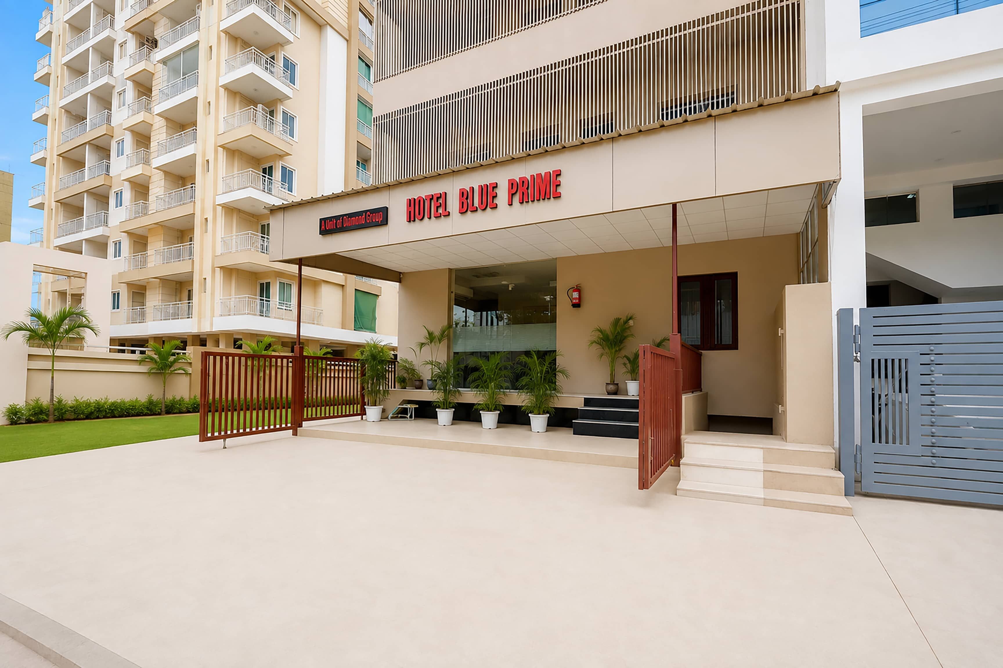 Entrada de un hotel con un cartel que dice 'HOTEL BLUE PRIME' y un camino de acceso con portones.