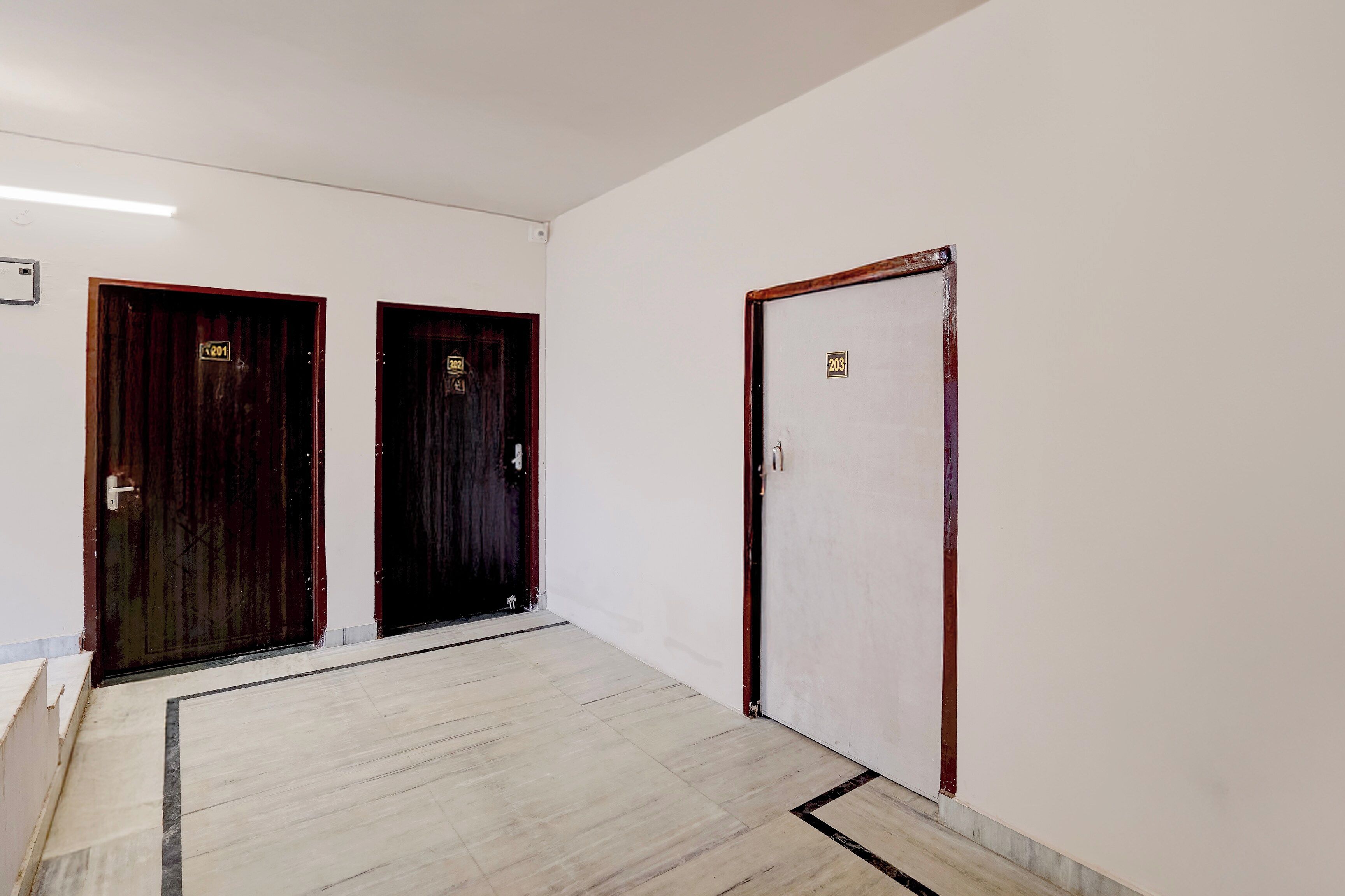 Un pasillo con tres puertas, dos de madera oscura y una blanca.
