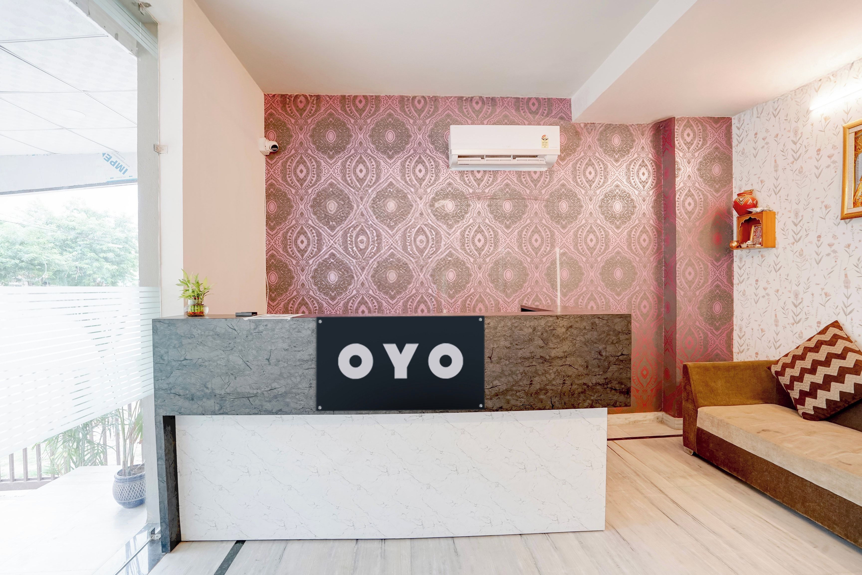 Una recepción con un cartel que dice 'OYO' en un interior moderno con papel tapiz estampado y un sofá.