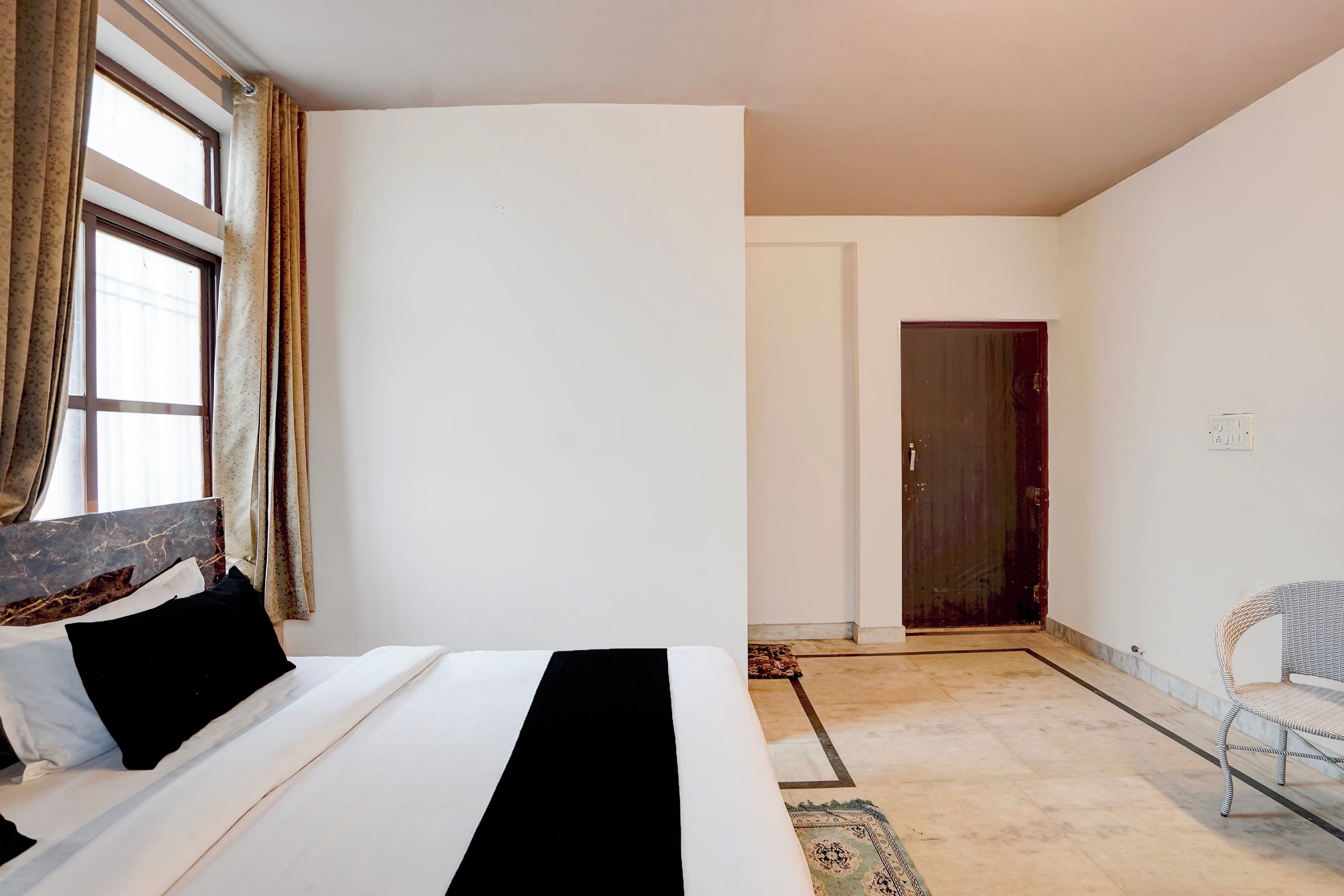 A bedroom with a bed, a chair, a door, and a window with curtains.