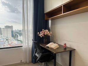 Una habitación con escritorio, silla y vistas a un paisaje urbano a través de una ventana con cortinas.