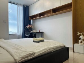 A hotel room with a bed, a desk, a chair, a window with curtains, and a view of the city. - RiverGate Suite – Upscale Apartment Near Ben Thanh Market (Thành phố Hồ Chí Minh)
