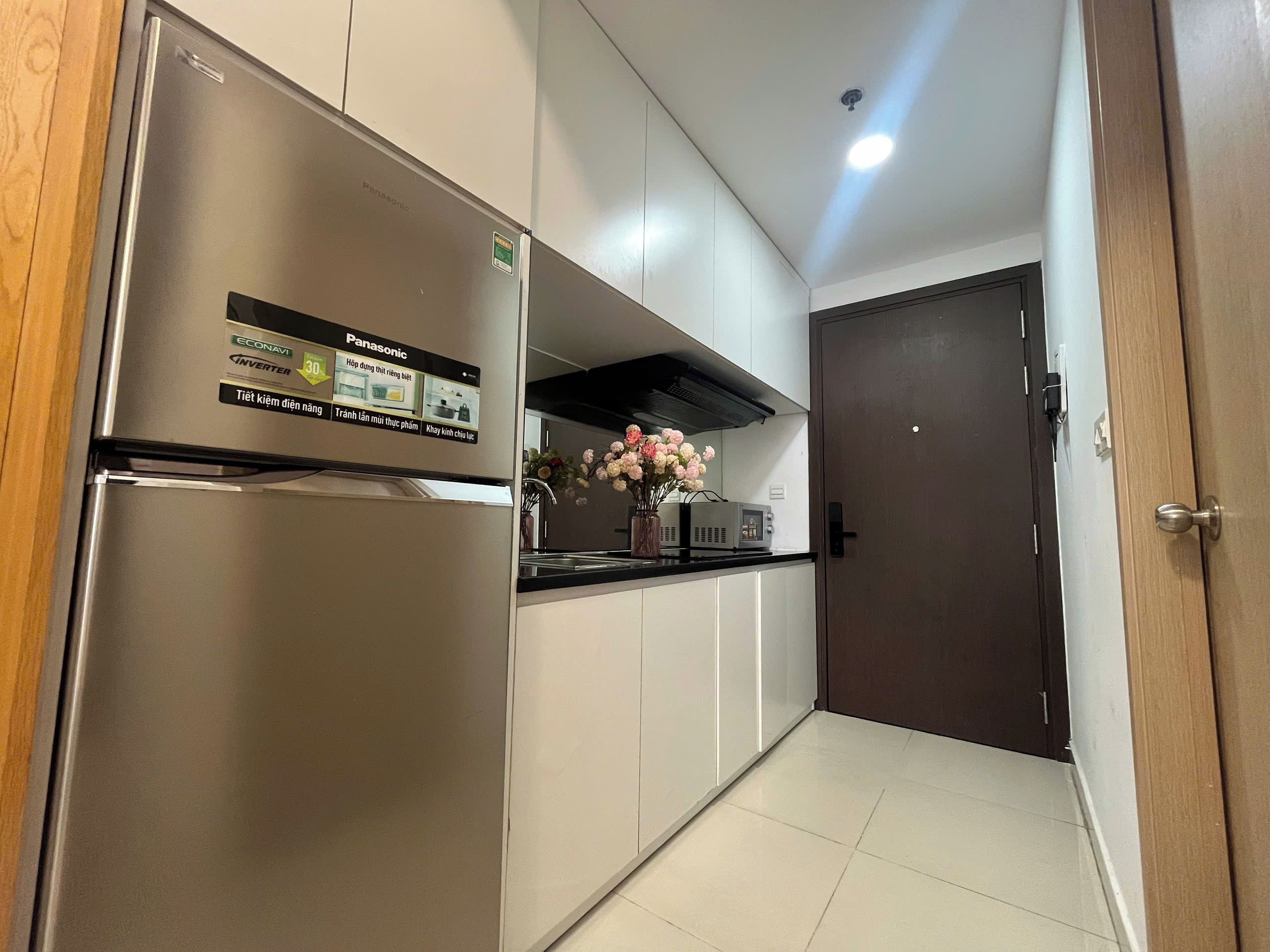 A modern kitchen with a stainless steel refrigerator, white cabinets, a black countertop, and a dark wooden door.