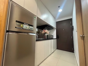 A modern kitchen with a stainless steel refrigerator, white cabinets, a black countertop, and a dark wooden door. - RiverGate Suite – Upscale Apartment Near Ben Thanh Market (Thành phố Hồ Chí Minh)